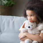 Young black girl hugs teddy bear toy